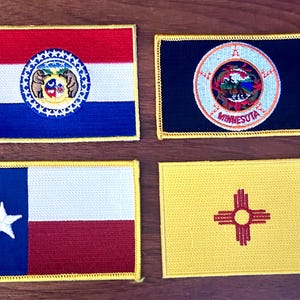 May include: Four rectangular embroidered patches featuring state flags. The Missouri patch has red, white, and blue stripes with a central emblem. The Minnesota patch is navy blue with a circular emblem. The Texas patch has a white star on blue and red and white stripes. The New Mexico patch is yellow with a red symbol.