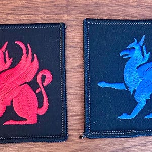 May include: Two square patches with embroidered griffin designs. One patch features a red griffin on a black background, while the other has a blue griffin. Both patches have a stitched border.
