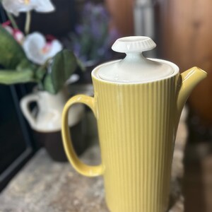May include: A yellow ceramic coffee pot with a white lid and a ribbed design. The pot has a handle and a spout.