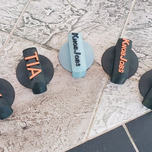 May include: Five black plastic knobs with different colored text. The text on the knobs reads "KnobJobs", "TIA", "BK", "KnobJobs", and "KnobJobs".
