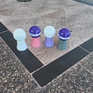 以下が含まれることがあります： 紫色の蓋と白いラベルが付いた、カラフルな小さな丸いプラスチック容器が4つあります。容器はタイル張りの床の上に置かれています。