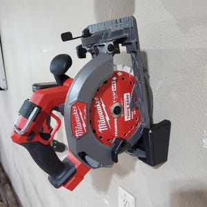 May include: A red and grey Milwaukee FUEL circular saw mounted on a wall. The saw blade is red with black text, and the saw has a black handle. The saw blade is 18.4 cm in diameter.