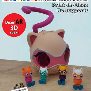 Puede incluir: Un contenedor con forma de gato impreso en 3D con un asa rosa y varias pequeñas figuras de gato. El contenedor es beige con detalles rosas y plateados. Las figuras son de varios colores. El texto en la imagen incluye "MULTICOLOR", "Print-in-Place" y "STL".