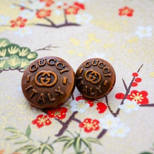 May include: Two brown, round buttons with the words "GUCCI ITALY" embossed in gold lettering.