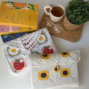 Puede incluir: Dos bolsas de crochet blancas con dise&ntilde;os florales y de girasoles. Las bolsas est&aacute;n hechas con hilo blanco y presentan flores coloridas, fresas y girasoles.