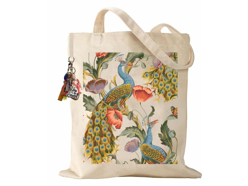 Peut inclure: Sac fourre-tout en toile de couleur cr&egrave;me avec un motif de paon et de fleurs. Le motif comprend des paons bleus, des coquelicots rouges et des feuilles vertes. Le sac a une poign&eacute;e assortie et un porte-cl&eacute;s avec des breloques color&eacute;es.