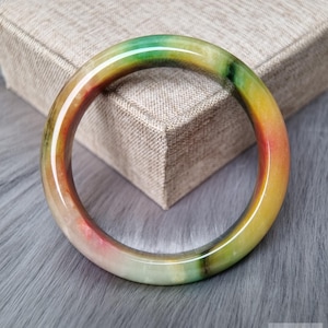 Op de afbeelding: Een gladde, ronde armband gemaakt van gepolijste steen, met een levendig kleurverloop van doorschijnend wit, dieprood, heldergeel en bosgroen, waarbij natuurlijke minerale insluitingen over het gehele oppervlak zichtbaar zijn.
