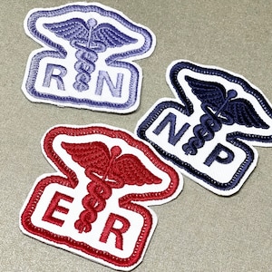 May include: Three embroidered patches featuring the medical symbol of a snake wrapped around a staff with wings. The patches are white with blue, red, and navy blue stitching. The patches read "RN", "NP", and "ER".