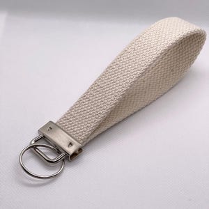May include: A white canvas key chain with a silver metal key ring and a silver metal clasp.