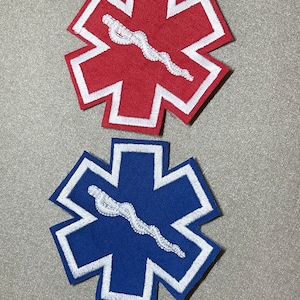 Puede incluir: Dos parches médicos bordados, uno rojo y otro azul, con un símbolo de serpiente blanca en el centro. Los parches tienen forma de estrella de seis puntas.