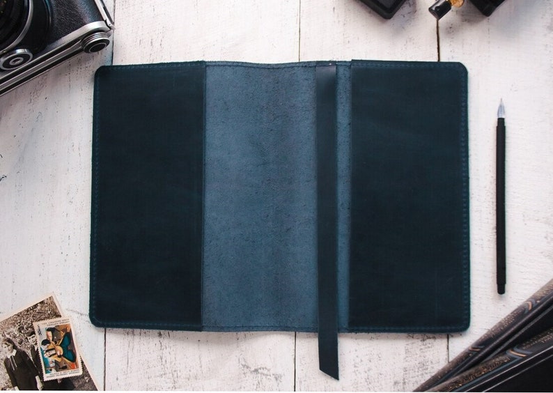 May include: A dark blue leather journal with a ribbon bookmark. The journal is open to reveal the blank pages inside.