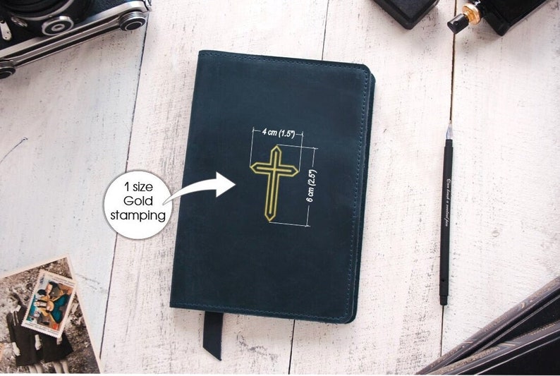 May include: A dark blue leather-bound journal with a gold cross embossed on the front cover. The cross is 1.5 inches wide and 2.5 inches tall. The journal has a black ribbon bookmark.