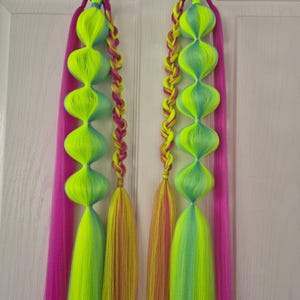 Puede incluir: Dos juegos de extensiones de cabello de colores con mechones rosas, amarillos y azules. Cada juego tiene una sección trenzada y una sección con grandes bucles redondos y coloridos.
