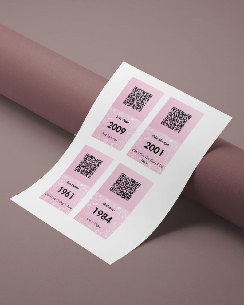 Pode incluir: Uma folha branca com quatro autocolantes cor-de-rosa e brancos. Cada autocolante apresenta um c&oacute;digo QR, o nome do artista, o ano e o t&iacute;tulo da m&uacute;sica. Os artistas s&atilde;o Lady Gaga, Kylie Minogue, Elvis Presley e Madonna. Os anos s&atilde;o 2009, 2001, 1961 e 1984. As m&uacute;sicas s&atilde;o 'Bad Romance', 'Can't Get You Out of My Head', 'Can't Help Falling in Love' e 'Like a Virgin'.