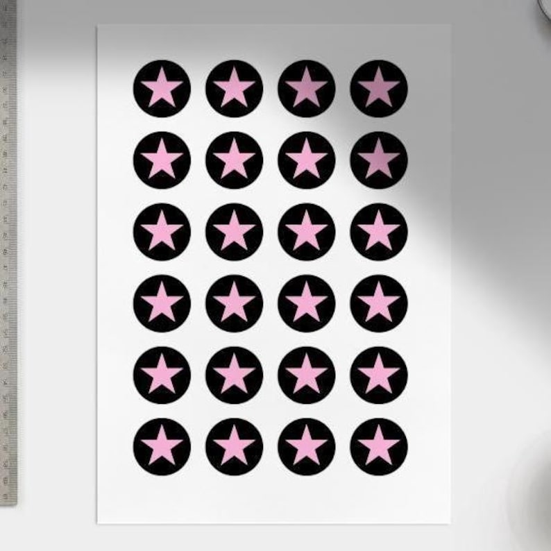 May include: A white sheet with a repeating pattern of black circles, each with a pink star. The circles are arranged in a grid. The stars are a lighter shade of pink. The design is simple and symmetrical.