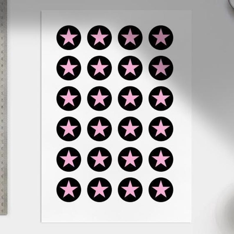 Puede incluir: Una hoja blanca con un patr&oacute;n repetitivo de estrellas rosas dentro de c&iacute;rculos negros. Las estrellas son de cinco puntas y est&aacute;n centradas en los c&iacute;rculos. El dise&ntilde;o est&aacute; espaciado uniformemente en el papel.