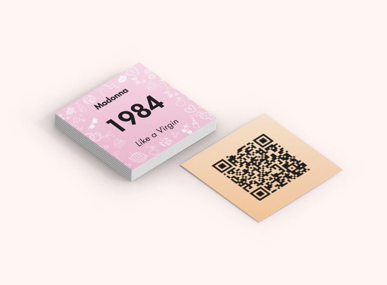Puede incluir: Una pila de tarjetas cuadradas rosas con el texto "Madonna 1984 Like a Virgin" e iconos decorativos. Al lado, una tarjeta cuadrada de color beige con un c&oacute;digo QR negro.