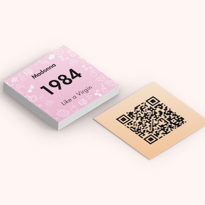 May include: A stack of pink square cards with the text "Madonna 1984 Like a Virgin" and decorative icons. Beside it is a square tan card with a black QR code.