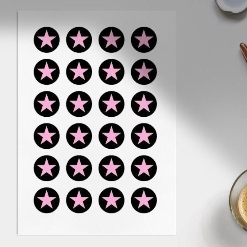 Pode incluir: Uma folha de autocolantes com estrelas cor-de-rosa dentro de c&iacute;rculos pretos. Os autocolantes est&atilde;o dispostos numa grelha sobre um fundo branco. As estrelas t&ecirc;m cinco pontas e s&atilde;o de cor rosa s&oacute;lida.