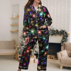 Könnte beinhalten: Schwarzes Pyjama-Set mit festlichem Weihnachtsmuster. Das langärmlige Oberteil und die Hose zeigen ein sich wiederholendes Design aus farbenfrohen Feiertags-Symbolen, darunter Glocken, Schneeflocken und Zuckerstangen. Weiße Paspeln am Kragen, an den Manschetten und an den Taschen.