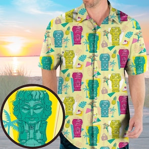 Pode incluir: Uma camisa de manga curta com um padrão repetido de estátuas tiki coloridas, abacaxis e elementos tropicais em um fundo amarelo claro. A camisa tem uma gola clássica e um ajuste relaxado, ideal para um look casual de verão.