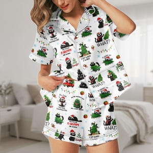 Peut inclure: Ensemble de pyjama de Noël blanc avec un motif de chat noir et de sapin de Noël. Le haut à manches courtes et le short comportent des phrases comme "What?" et "I do what I want." L'ensemble a une bordure blanche et une fermeture boutonnée.