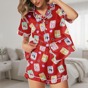 May include: Red pajama set featuring a repeating pattern of cartoon characters in cans, hearts, and stars. The short-sleeved top and shorts have white trim. The pajamas are made of a silky material.
