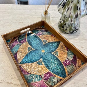 Könnte beinhalten: Ein Serviertablett aus Holz mit einem Mosaikdesign, das ein blaues, gelbes und rosafarbenes geometrisches Muster zeigt. Das Tablett hat einen Holzrahmen und eine klare Glasplatte.