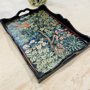 Puede incluir: Una bandeja de servir de madera negra con un dise&ntilde;o floral decorativo que presenta un p&aacute;jaro y una ardilla. La bandeja tiene dos asas a los lados.