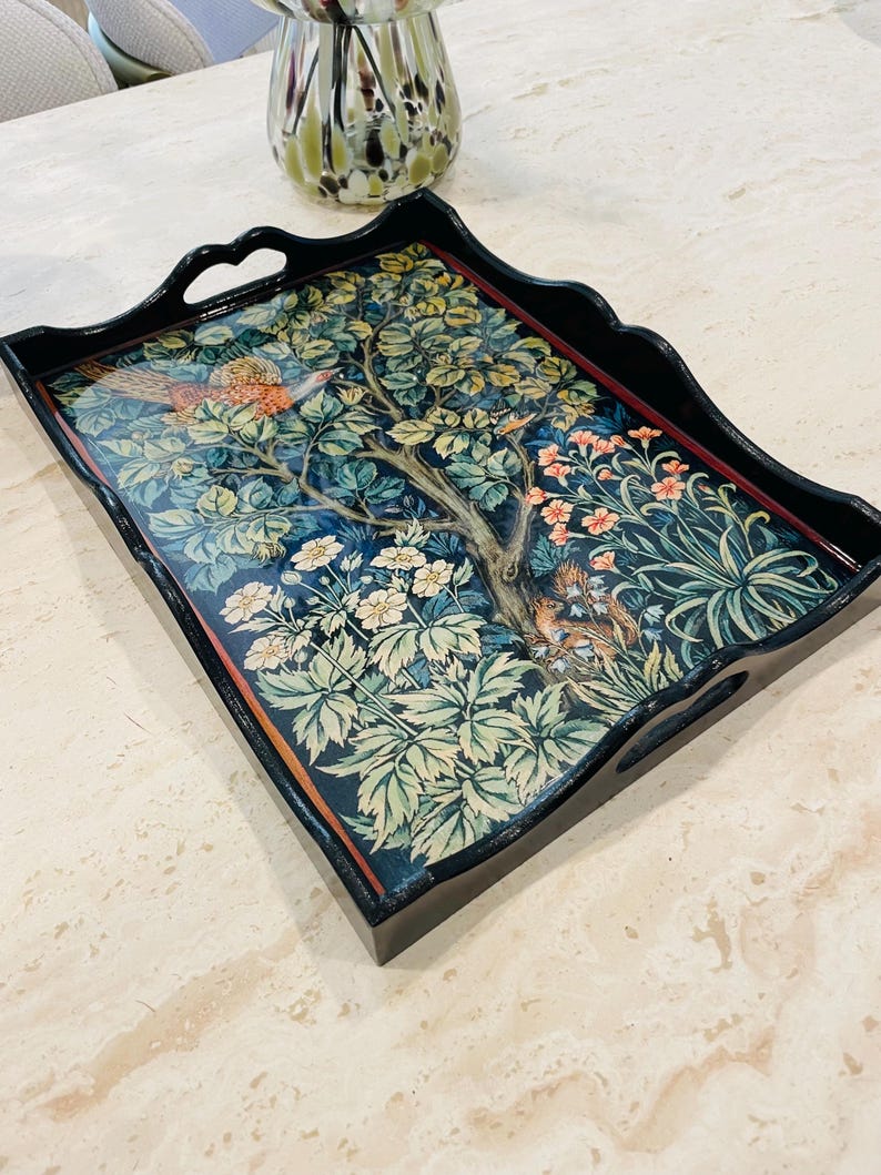 Puede incluir: Una bandeja de servir de madera negra con un dise&ntilde;o floral decorativo que presenta un p&aacute;jaro y una ardilla. La bandeja tiene dos asas a los lados.