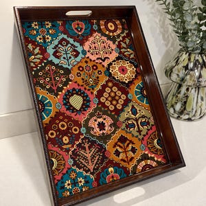 May include: A rectangular wooden serving tray with a dark brown polished finish and cutout handles. The base features a vibrant, multi-coloured floral and geometric pattern in shades of teal, mustard yellow, deep red, and pink.