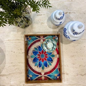 May include: A wooden serving tray with a colorful mosaic design featuring blue, red, and green colors. The tray has a small saucer and cup on top.