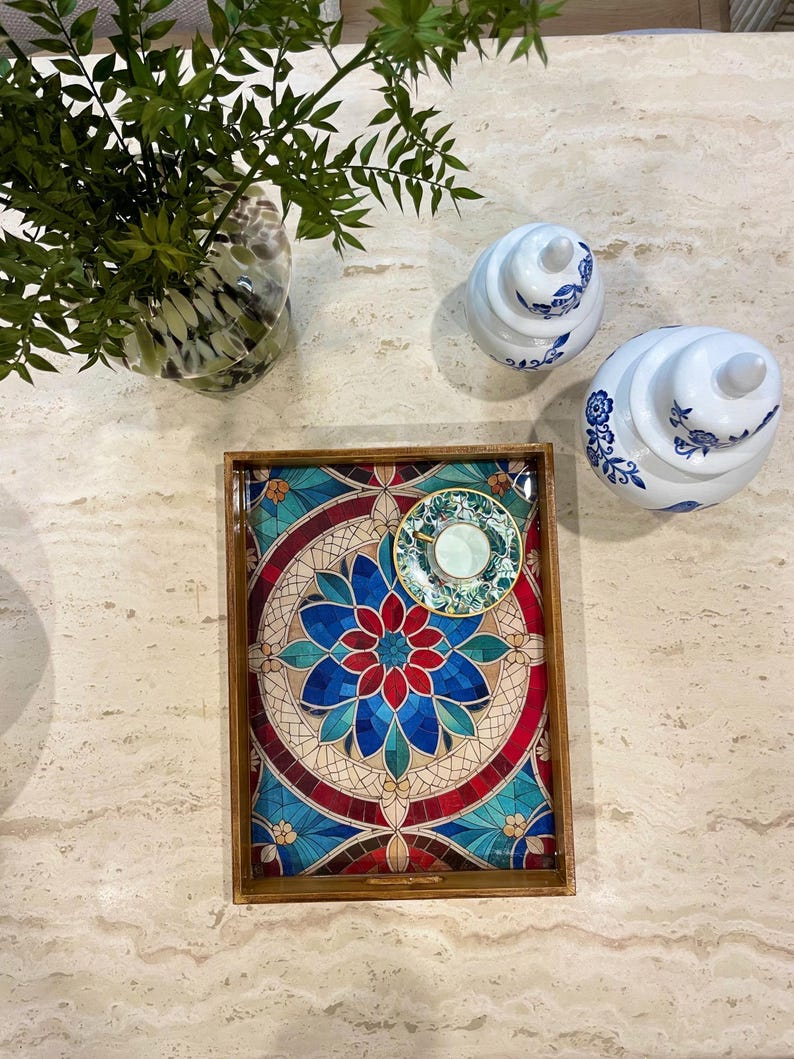 May include: A wooden serving tray with a colorful mosaic design featuring blue, red, and green colors. The tray has a small saucer and cup on top.