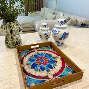 May include: A wooden serving tray with a colorful mosaic design featuring a blue, red, and green floral pattern. The tray has two handles on each side.