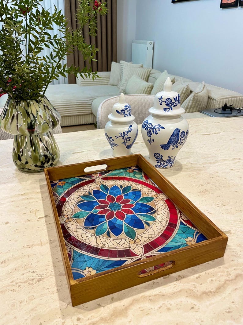 May include: A wooden serving tray with a colorful mosaic design featuring a blue, red, and green floral pattern. The tray has two handles on each side.