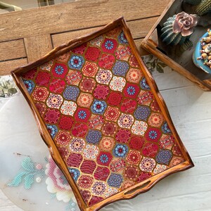 May include: A wooden serving tray with a decorative, colorful, geometric pattern. The tray has a brown wooden frame and a red, blue, and gold patterned surface.