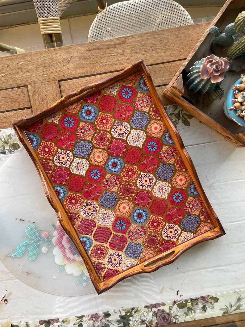 May include: A wooden serving tray with a decorative, colorful, geometric pattern. The tray has a brown wooden frame and a red, blue, and gold patterned surface.