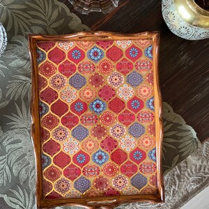 May include: A wooden serving tray with a decorative red, blue, and gold patterned design. The tray has a scalloped edge and a handle.