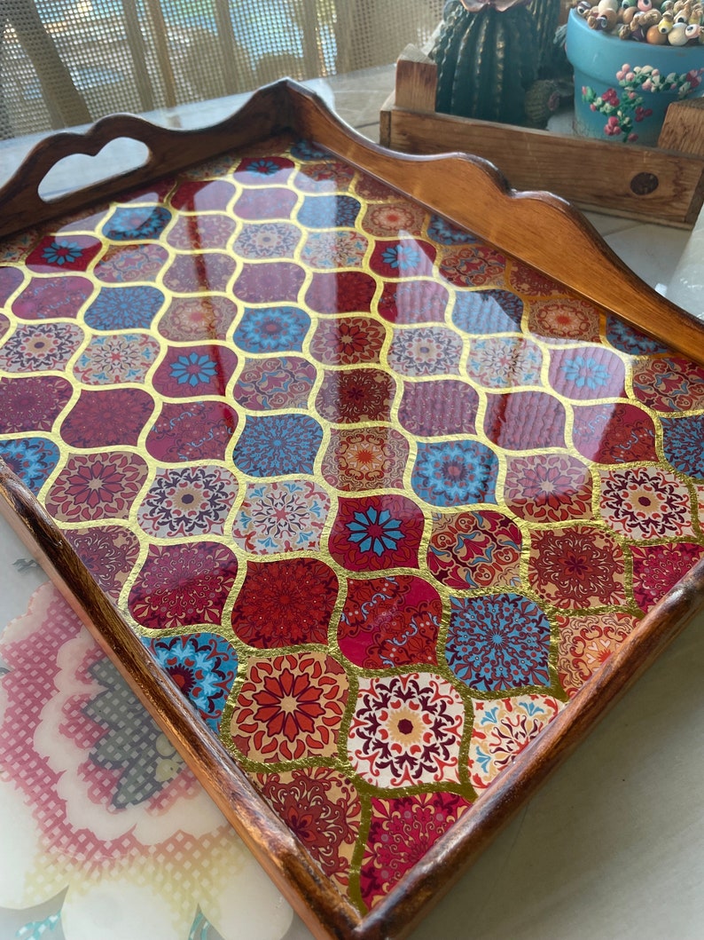 May include: A wooden serving tray with a decorative resin top. The resin top features a geometric pattern of red, blue, gold, and white. The tray has a handle on each side.