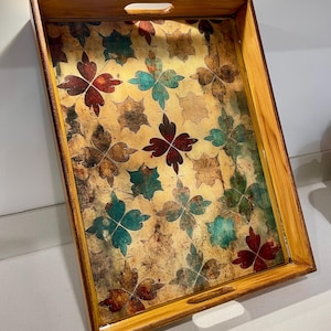 May include: Rectangular wooden serving tray with a floral pattern in shades of red, teal, and brown on a gold background. The tray has a light brown wooden frame with cut-out handles on each side.