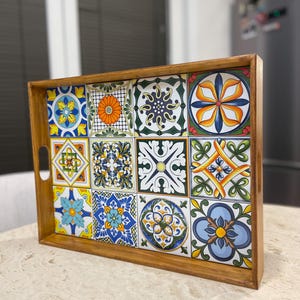 May include: A wooden serving tray with a colourful tile design. The tiles feature a variety of geometric patterns and floral motifs in shades of blue, green, yellow, orange, and white.