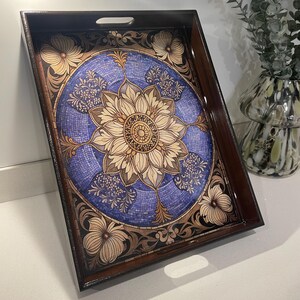 Könnte beinhalten: Rechteckiges Serviertablett aus Holz mit dunkelbraunem Rahmen. Das Tablett hat ein zentrales blaues Mosaikdesign mit einem floralen Mandala-Muster in Beige- und Brauntönen. Florale und Rankenmuster verzieren den Rand.