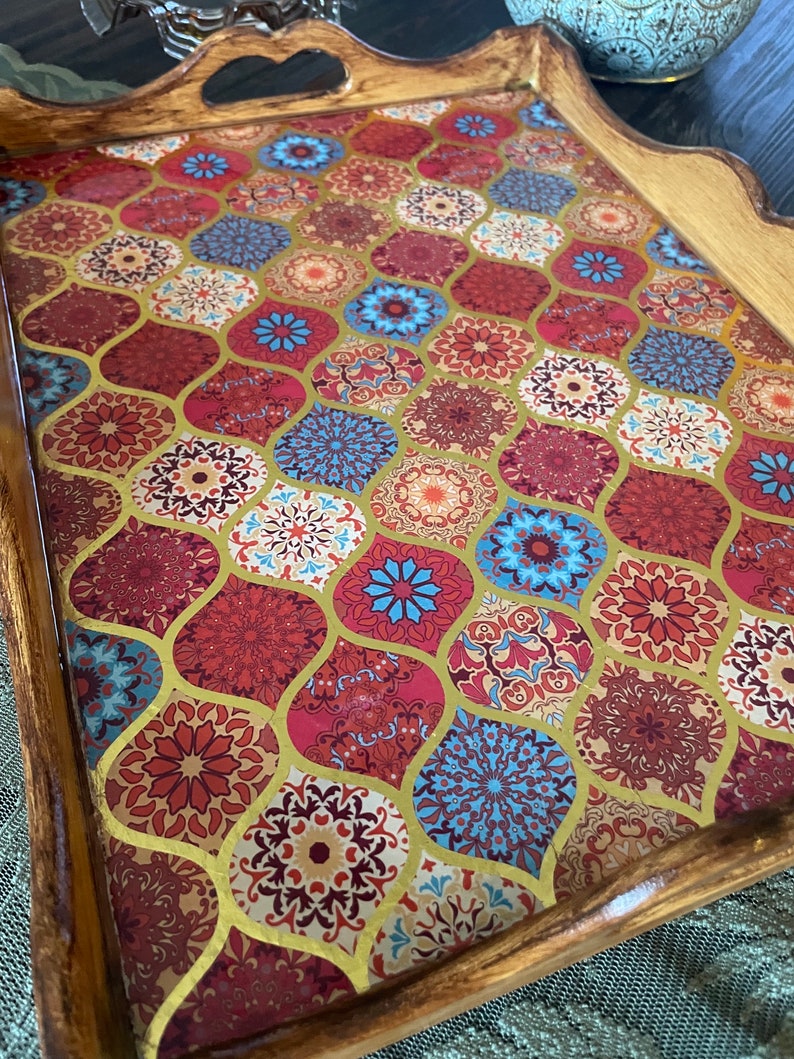 May include: A wooden serving tray with a decorative, colorful, geometric pattern. The tray has a handle and a scalloped edge.