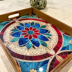 May include: A wooden serving tray with a colorful mosaic design featuring blue, red, and green tones. The mosaic design is reminiscent of stained glass.