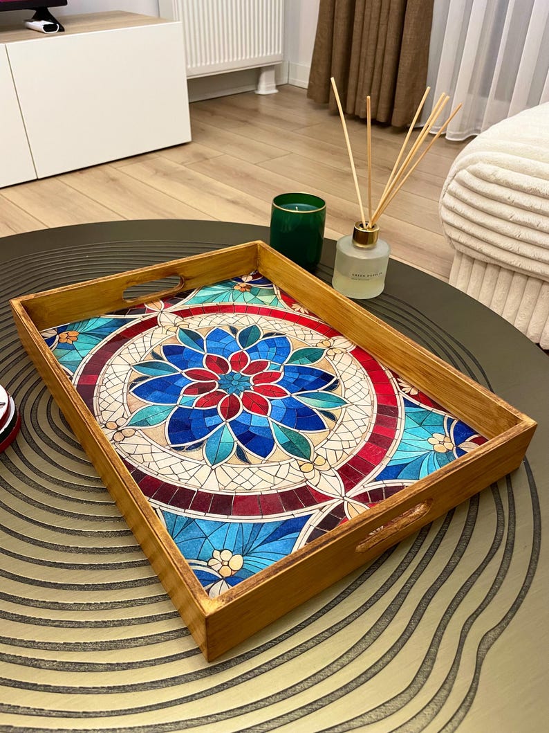 May include: A wooden serving tray with a colorful mosaic design featuring a blue, red, and green floral pattern. The tray has two handles on the sides.