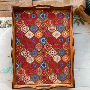 May include: A wooden serving tray with a decorative design featuring a geometric pattern of red, blue, gold, and white. The tray has a brown wooden frame and two handles.