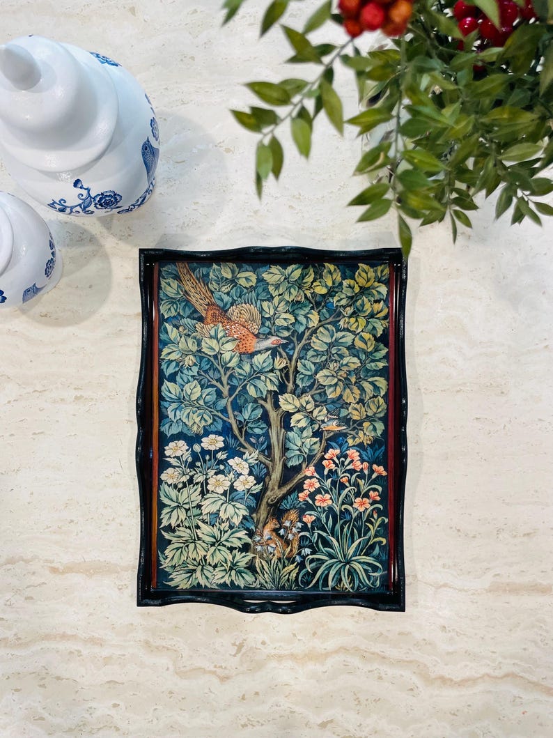 Puede incluir: Una bandeja de madera negra con un borde elevado presenta una impresi&oacute;n colorida de un p&aacute;jaro en un &aacute;rbol rodeado de flores y hojas. La bandeja tiene un marco de madera oscura.