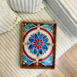 May include: A wooden serving tray with a stained glass design featuring a red, blue, and white circular pattern. The tray has a handle on one side.