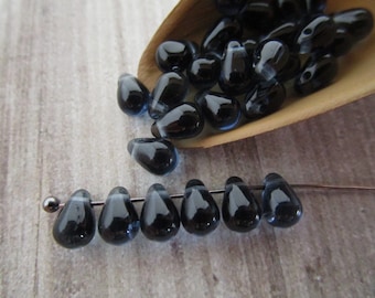 May include: A collection of dark blue glass teardrop beads with a white iridescent sheen. The beads are arranged in a wooden spoon and on a wire.