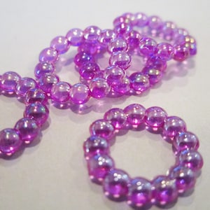 May include: A set of four iridescent purple beaded rings. The rings are made of small, round beads that are strung together to form a circle.